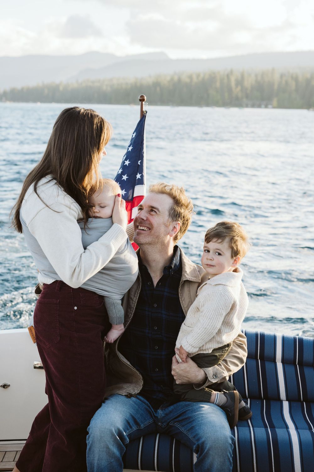 Family enjoying quality time on a boat with American flag and mountain backdrop.