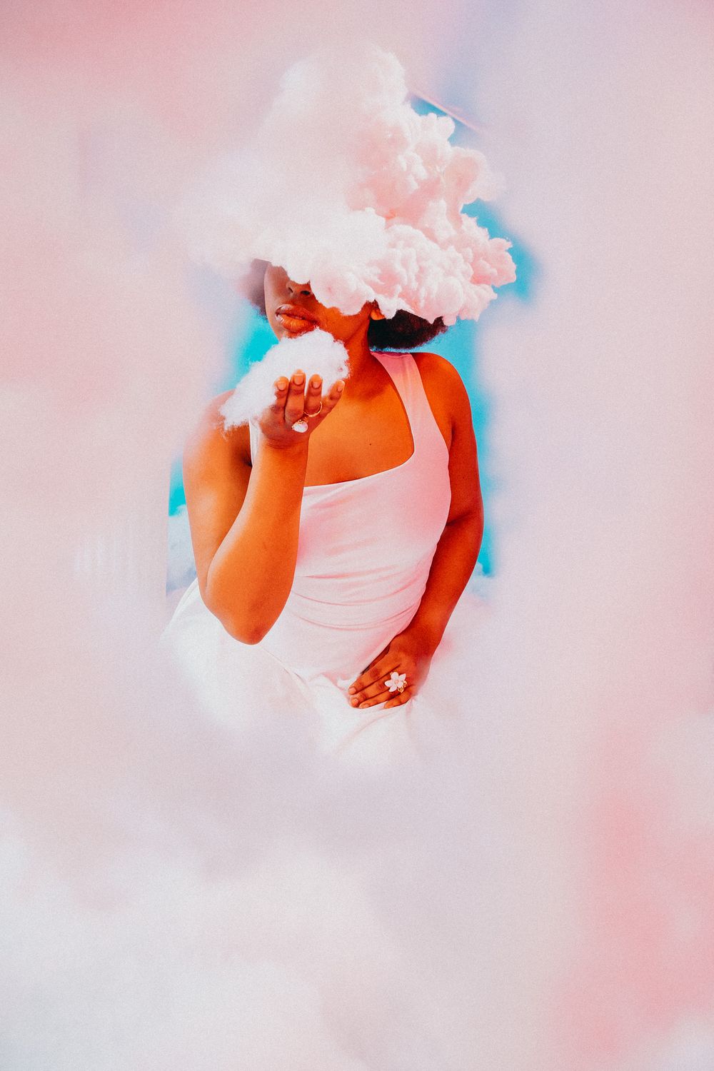 A person in a pink tank top surrounded by billowing pink and white smoke clouds against a pastel background.