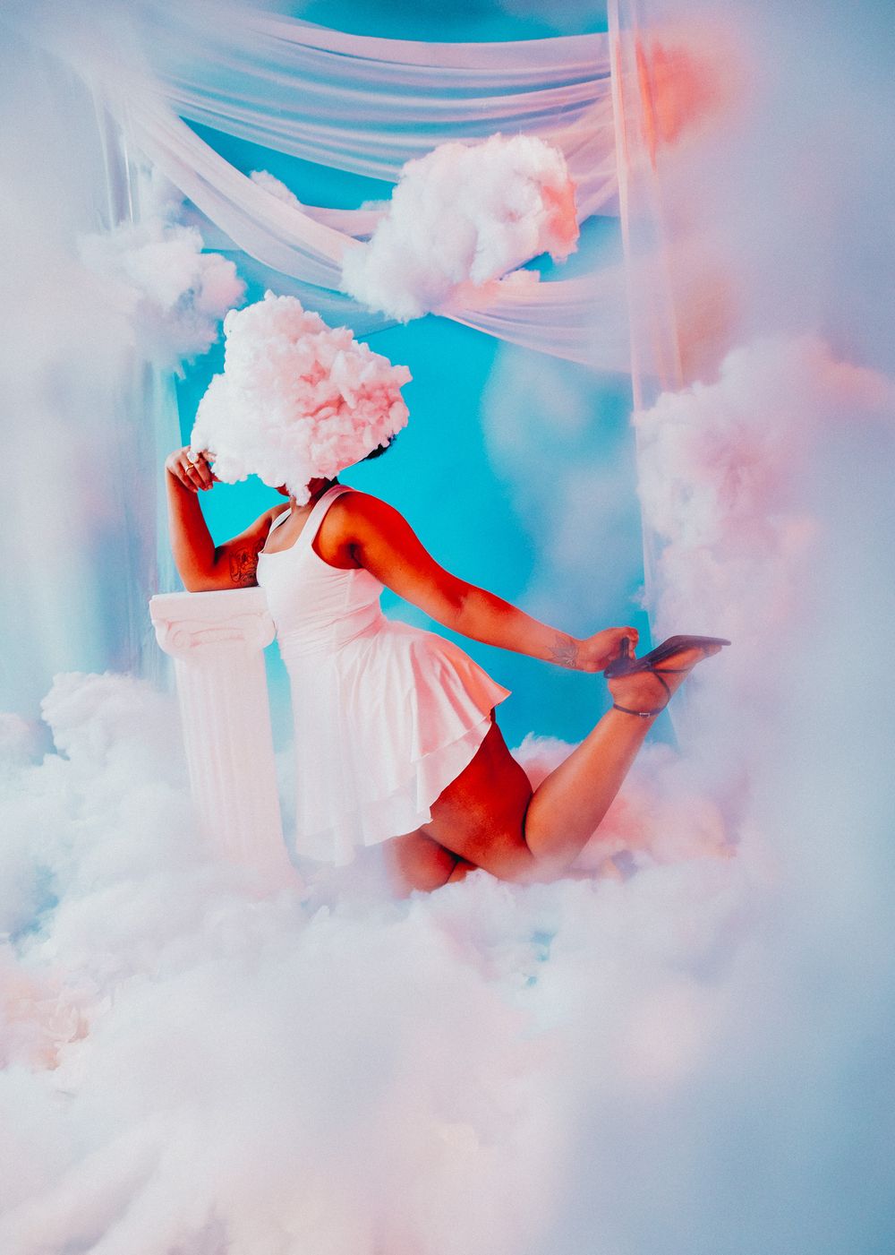 Dancer in white dress with cloud wig poses among fluffy clouds in dreamy blue sky-themed artistic photo.