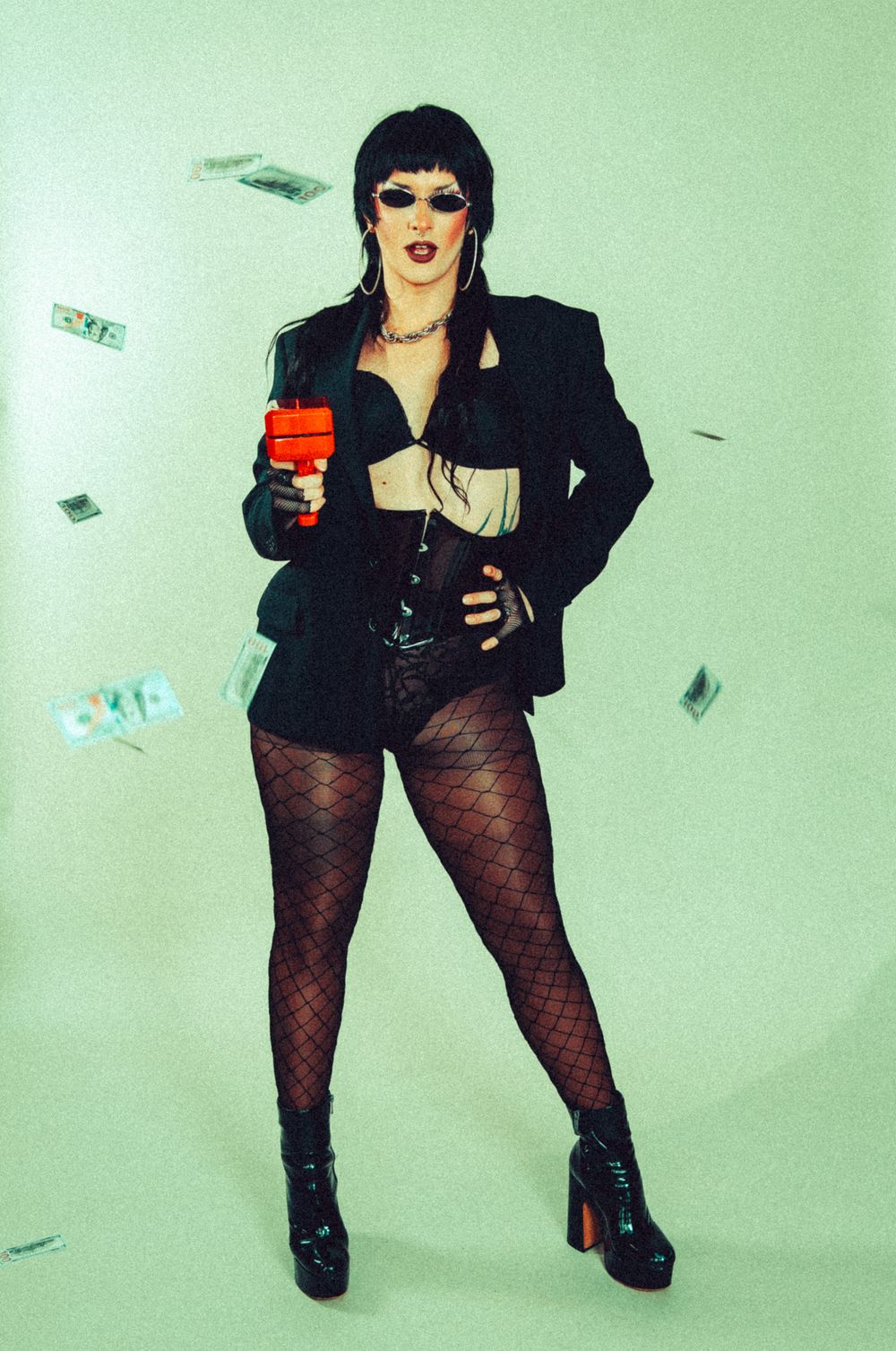 Edgy performer in black blazer shoots money gun with cash flying in studio.