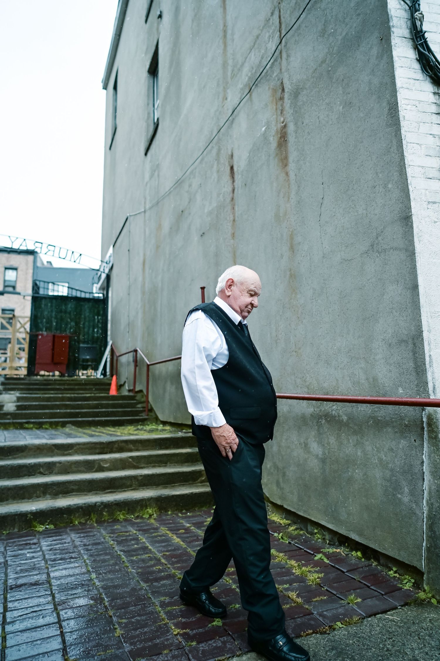 Bride’s father stepping down a stone staircase during the wedding, showing a complex expression against a concrete wall background.