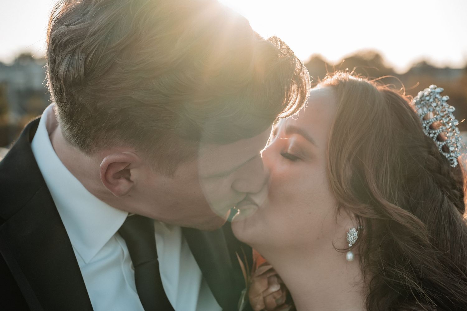 A romantic sunset moment between newlyweds sharing a tender kiss outdoors.