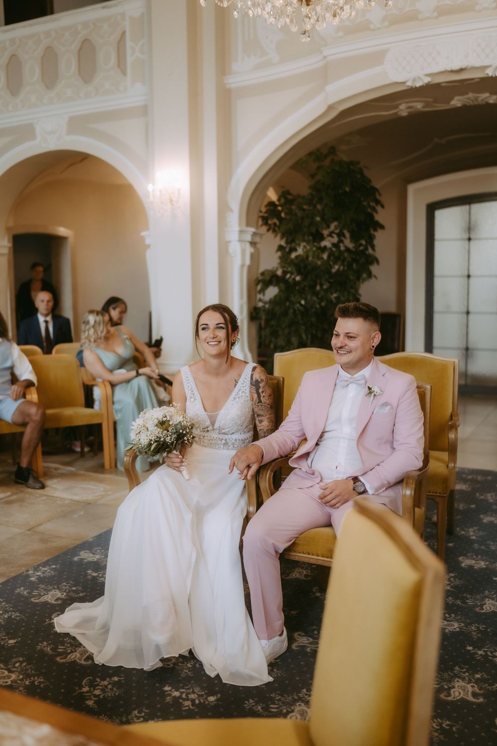Wedding guests seated in elegant ballroom with crystal chandeliers and marble details.