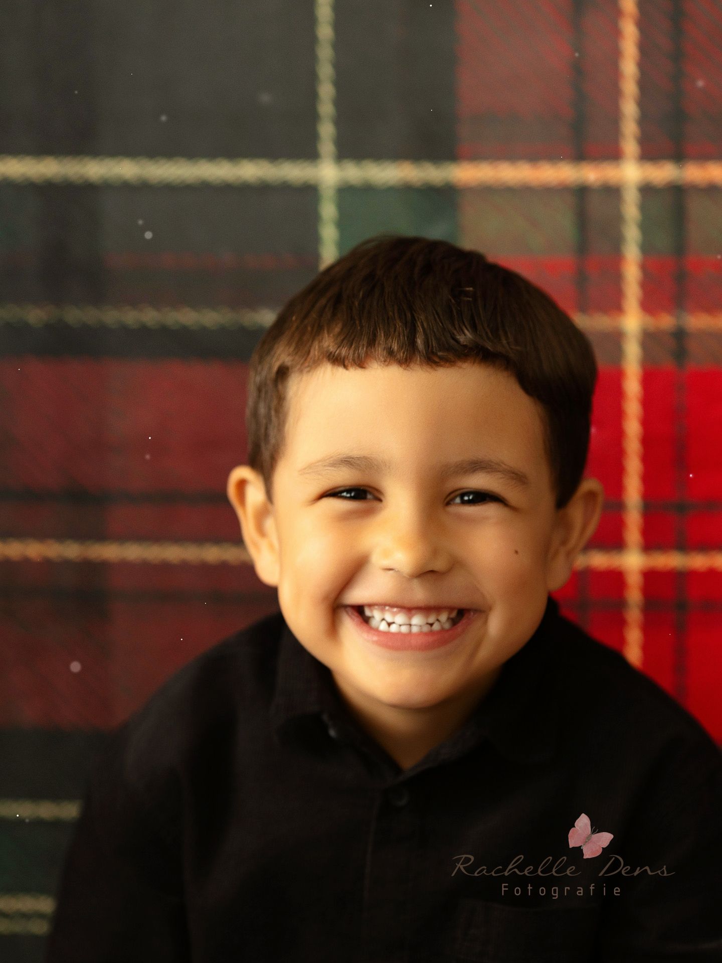 A joyful smile against a red plaid background wearing a black hoodie in a professional portrait photo.