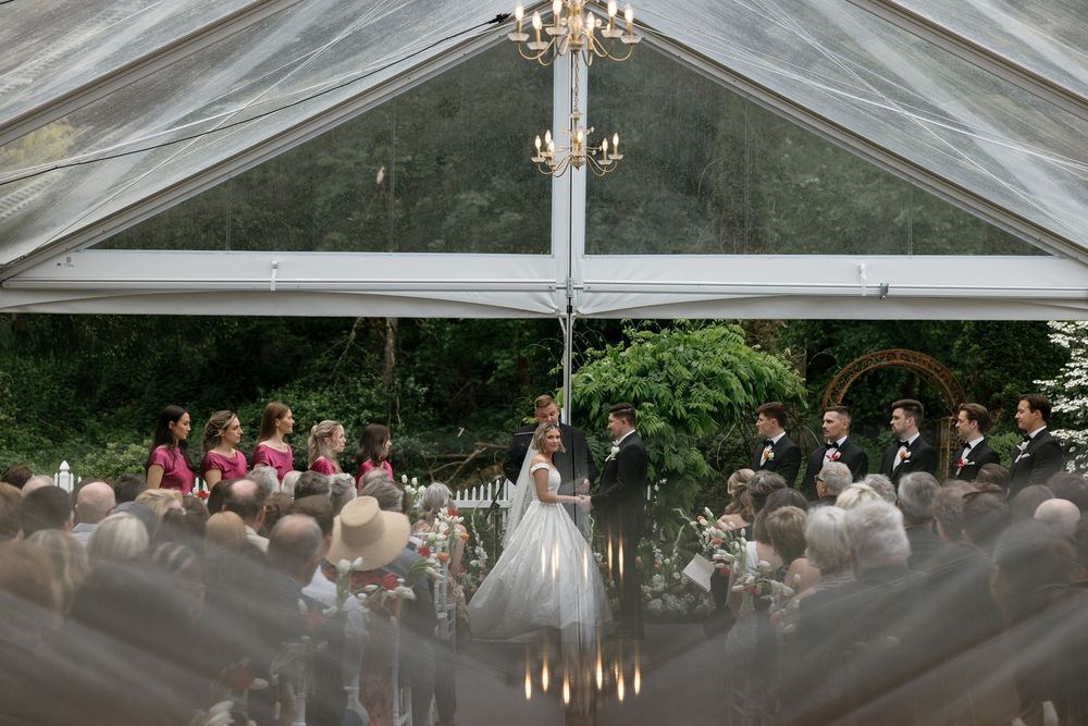 Elegant wedding ceremony setup under a white tent with chandeliers and rows of white chairs.