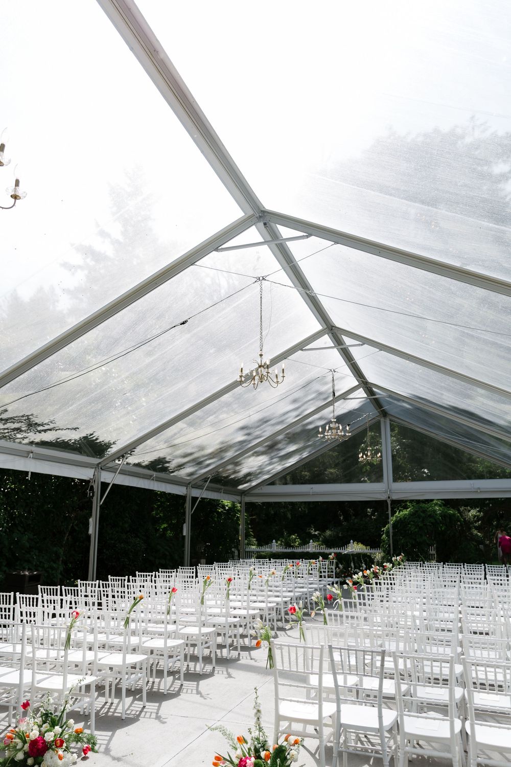 White chairs arranged in rows under a clear tent canopy for an outdoor wedding ceremony with floral decorations.