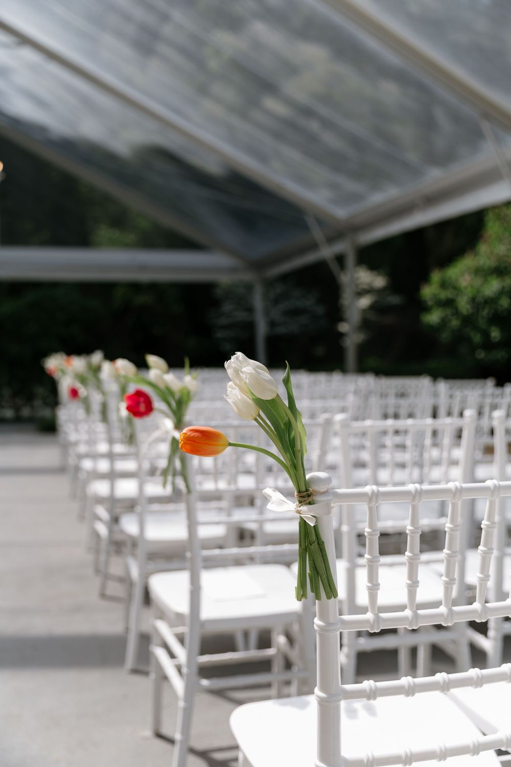 White wooden chairs arranged in rows for an outdoor wedding ceremony with delicate floral decorations on the aisle.