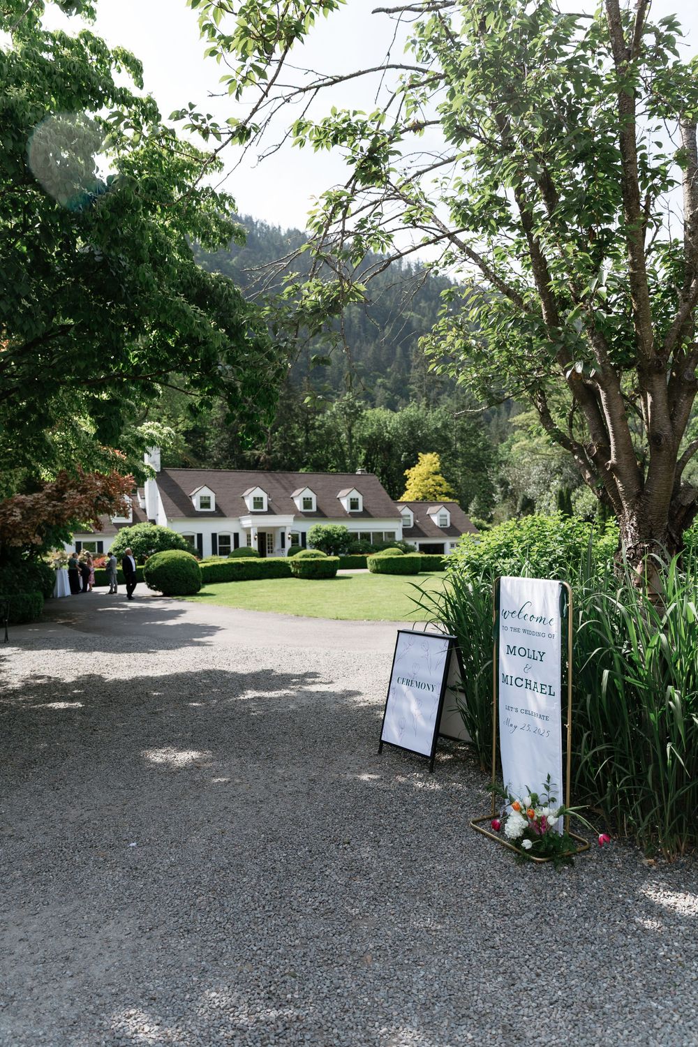 Gravel pathway leading to a white colonial style house with welcome signs and landscaping.