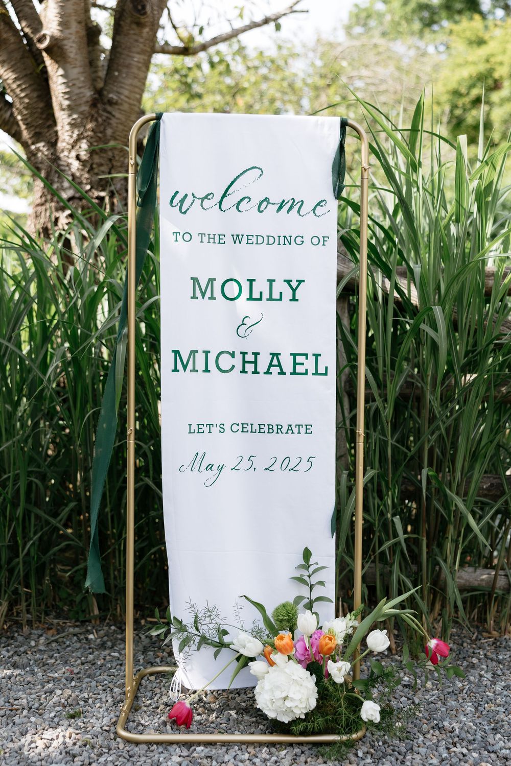 A series of elegant white wedding welcome signs decorated with greenery and flowers display event details in a garden setting.
