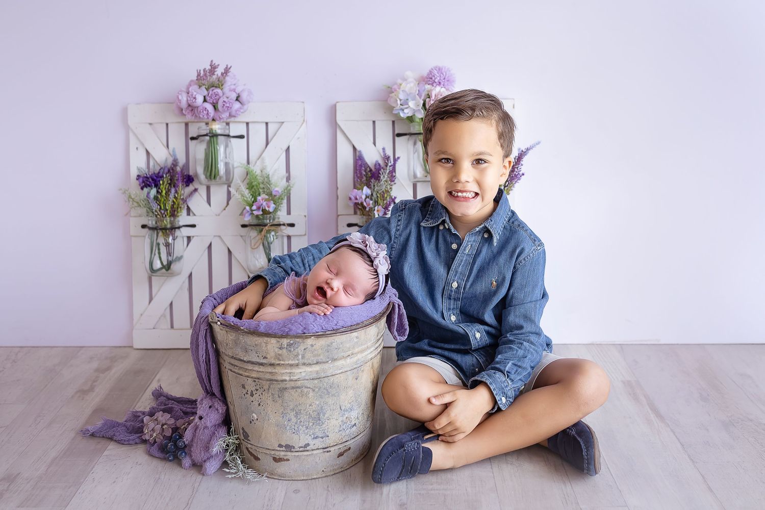 newborn baby inside a bucket smiling big brother sits beside her smiling with a proud expression