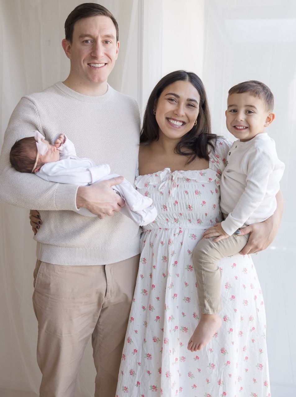 "Parents holding their newborn during in-home lifestyle session with sibling all smiling at the camera."