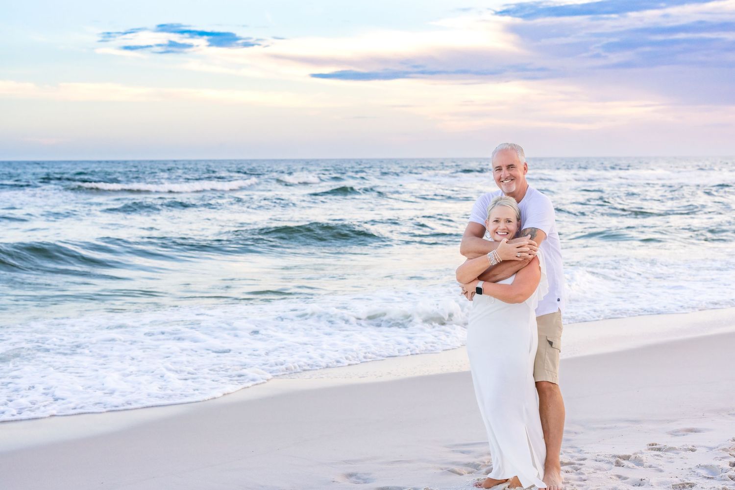 A person in a white dress walks along a scenic beach shoreline during a golden sunset.