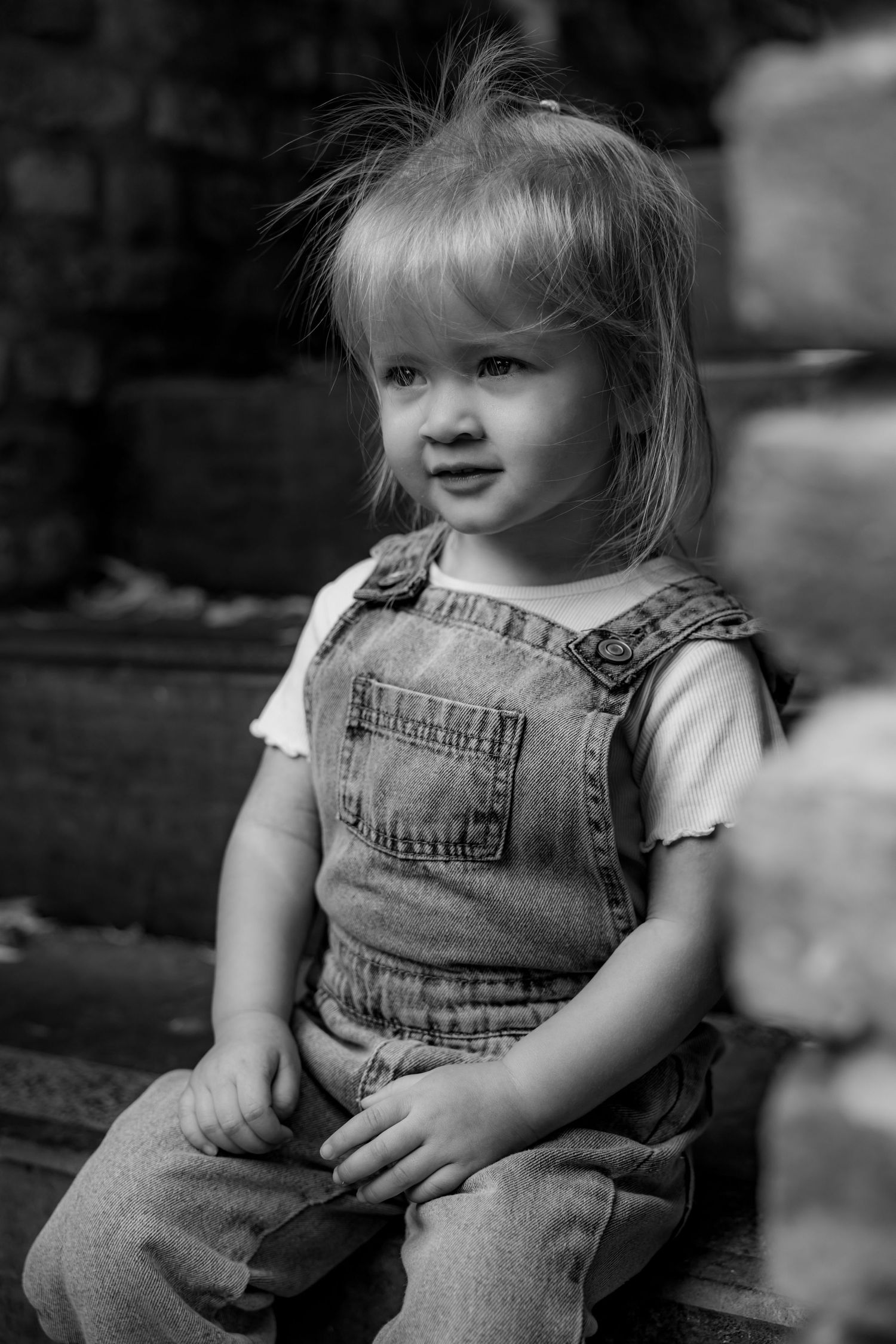 Black and white portrait series showing a toddler in denim overalls against a blurred background.