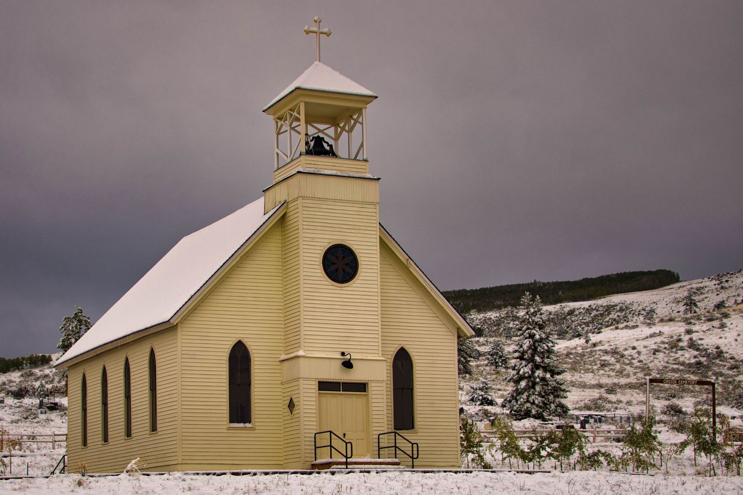A series of small yellow churches with steeples stand against a snowy winter landscape in rural America.