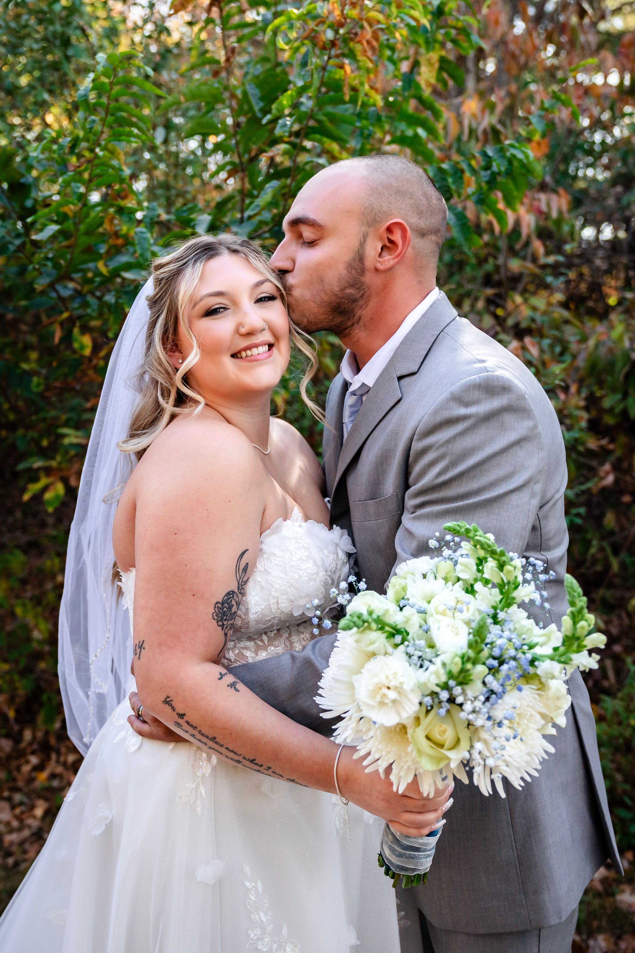 Bride holding white bouquet embraces groom during outdoor autumn wedding photoshoot.