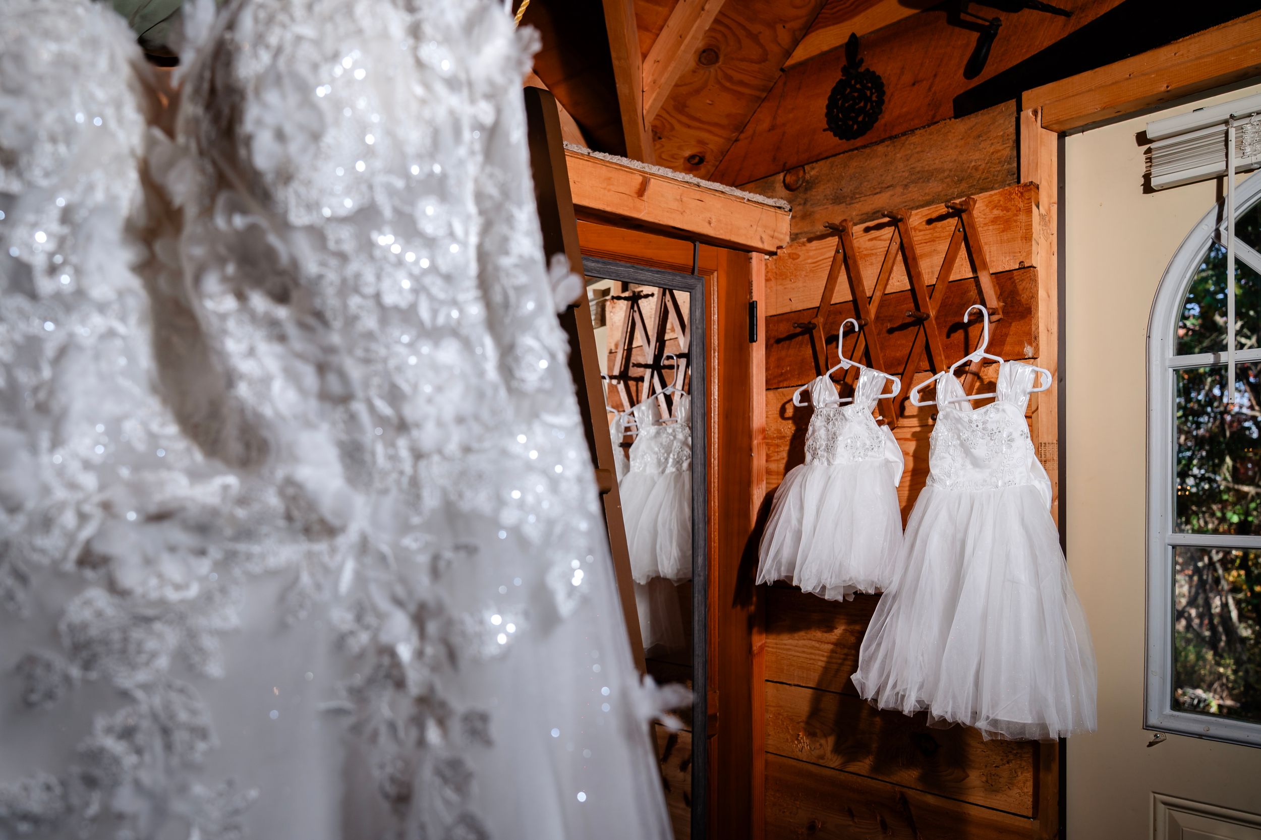 Wedding dress hanging in rustic wooden interior with warm lighting.