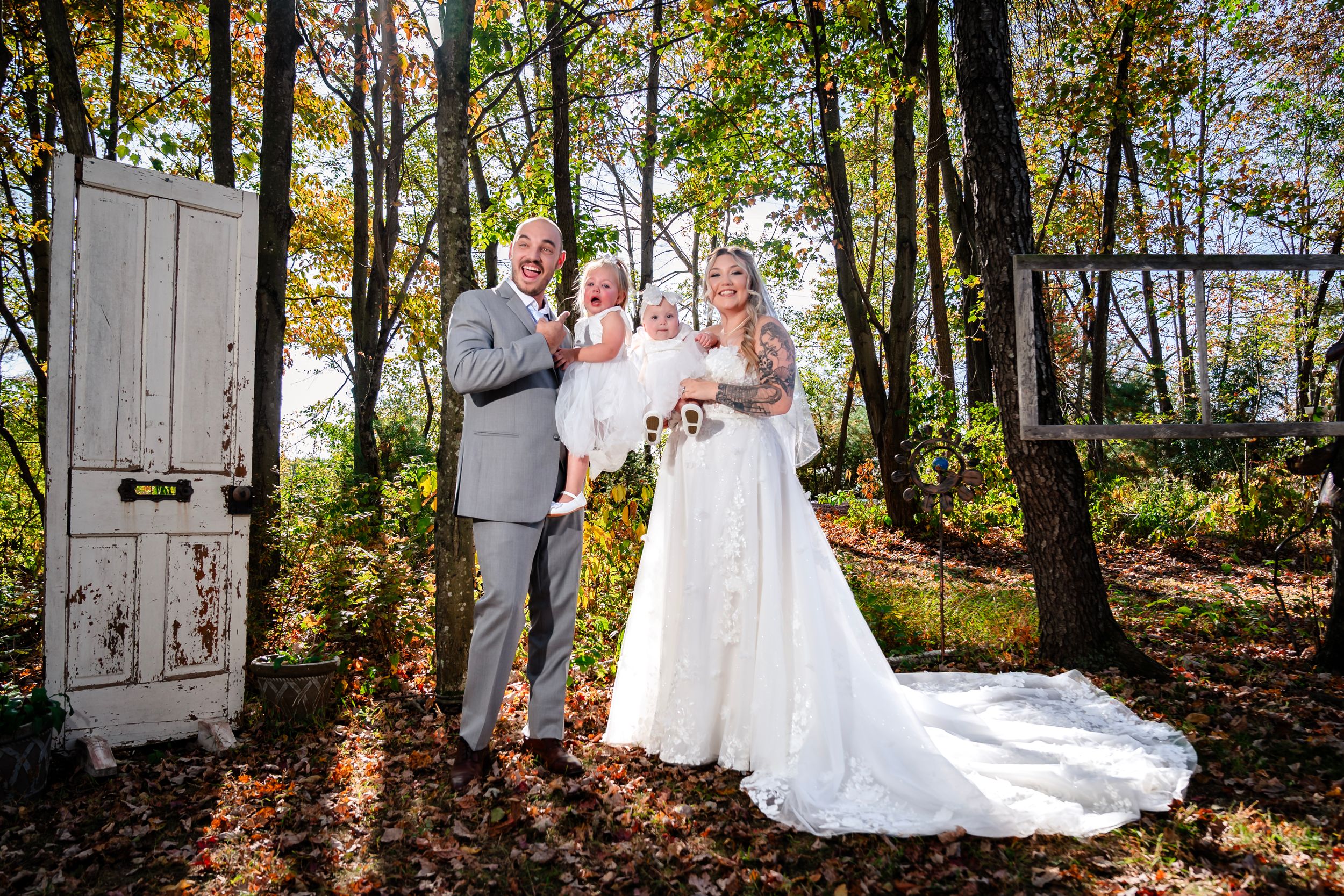 Wedding portraits taken in front of rustic white doors in a scenic wooded setting.