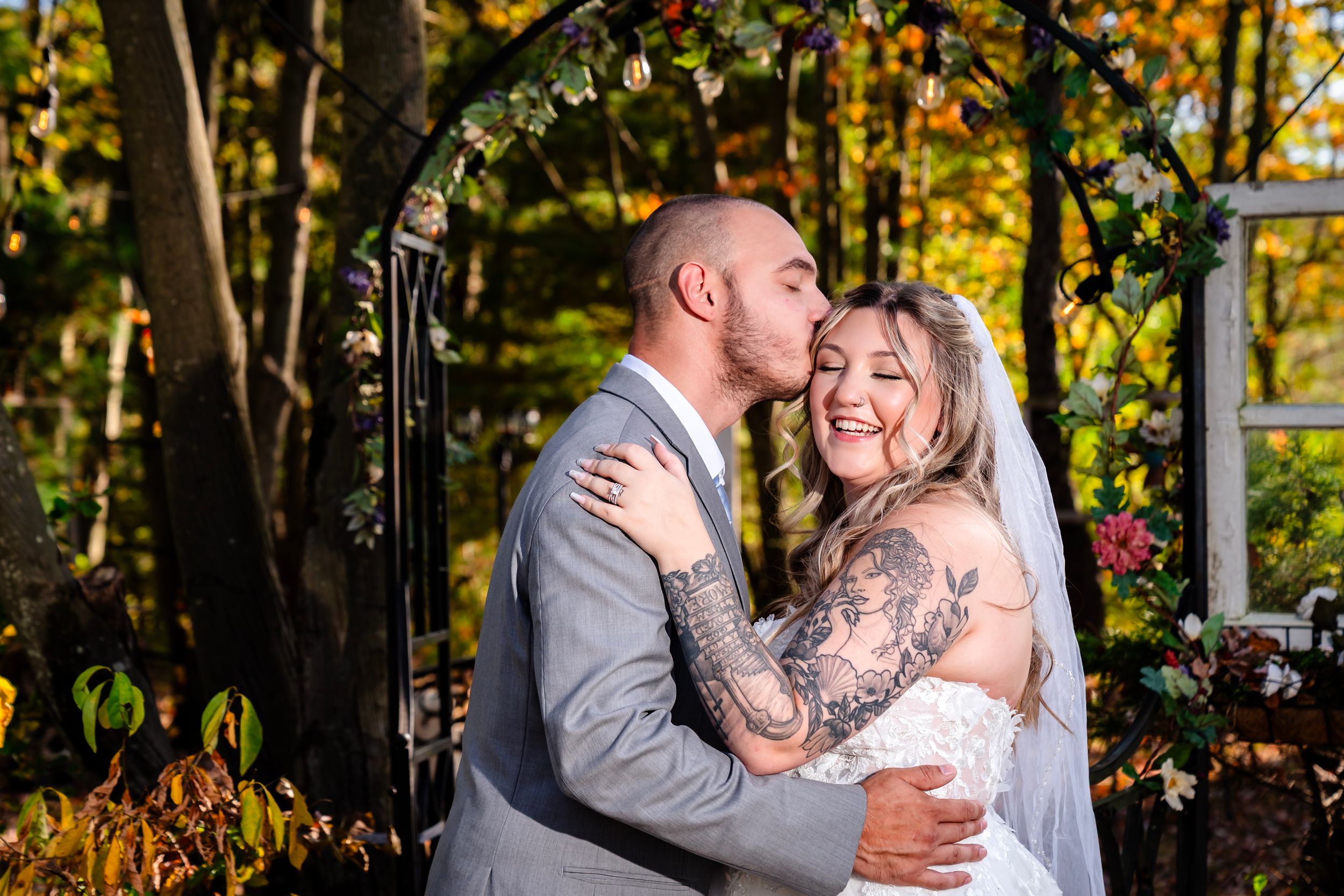 A joyful wedding moment captured under a decorated arch with fall foliage in the background.