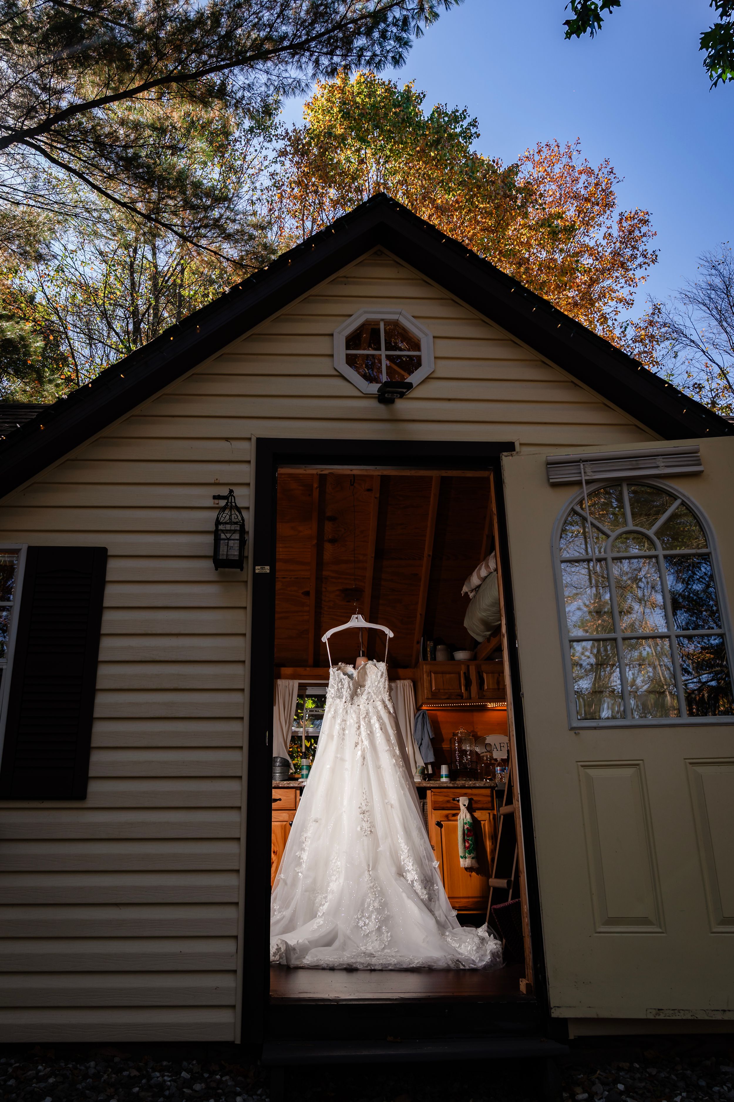 White wedding dress displayed against a small cottage exterior in autumn.