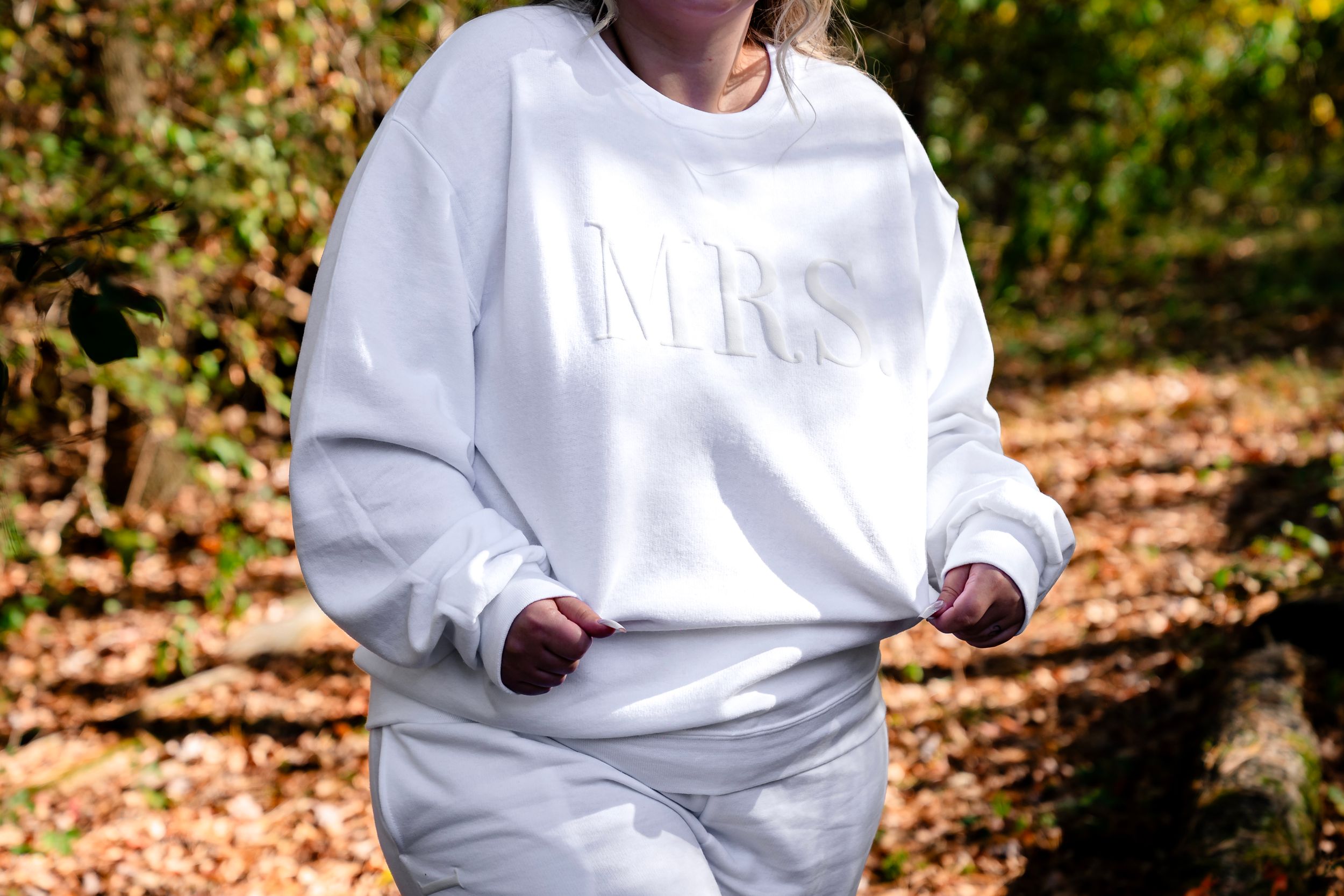 Person wearing white sweater walking through autumn forest setting.