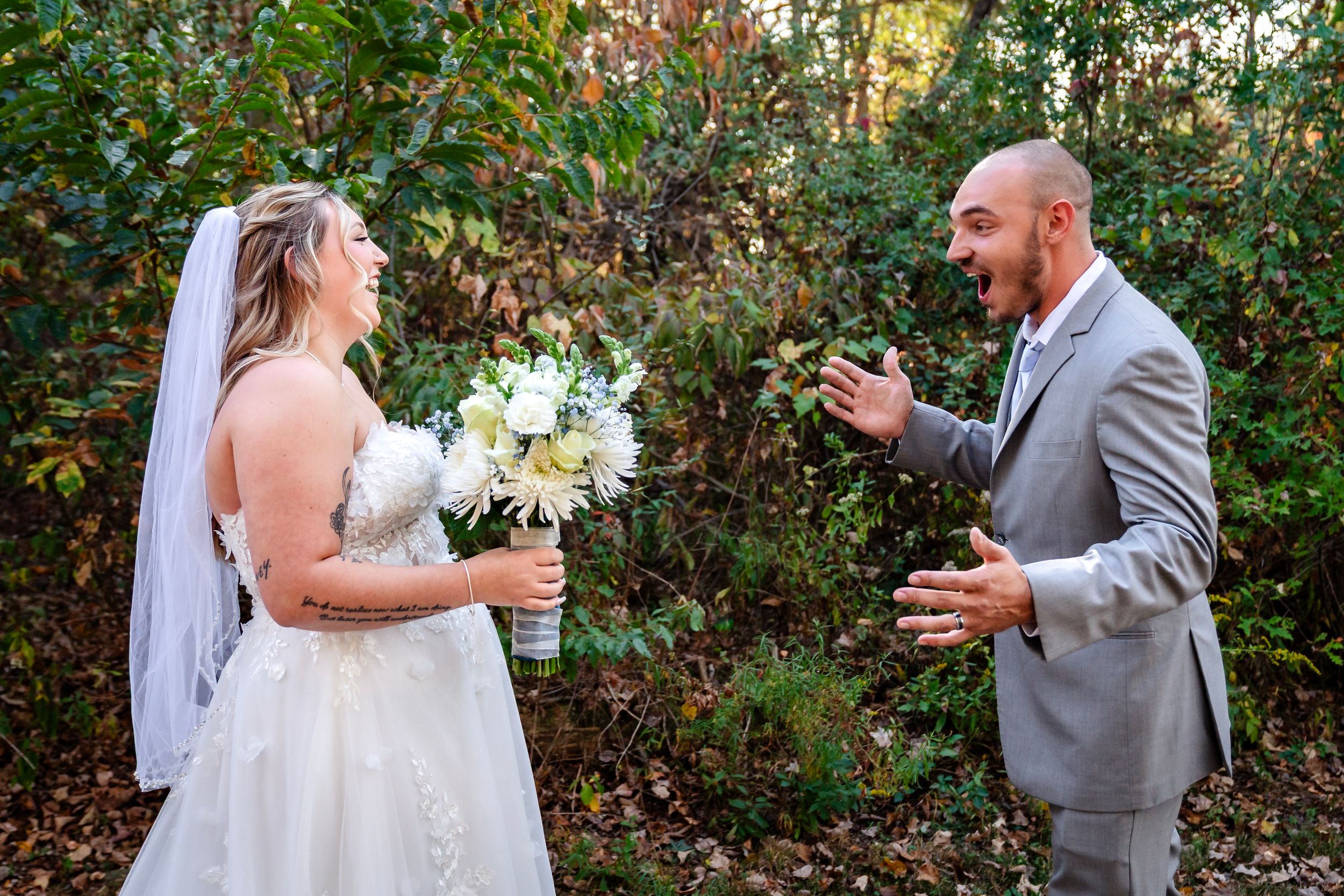 Wedding couple shares joyful reactions during their outdoor first look surrounded by fall foliage.