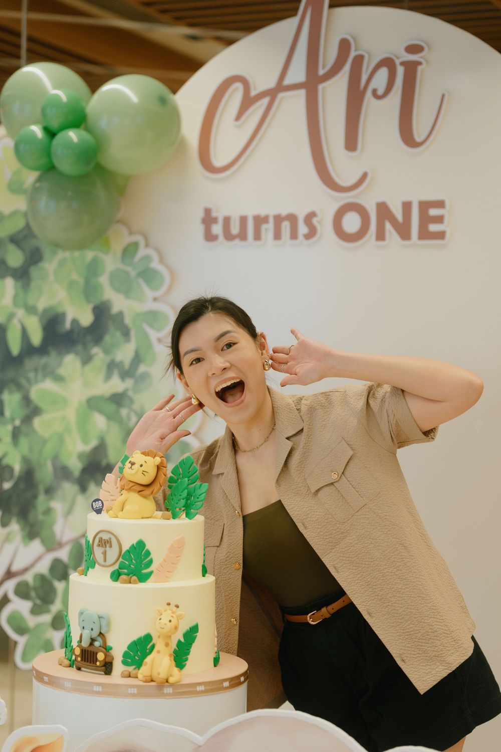 A festive first birthday celebration with a white and green decorated cake and balloon decorations.