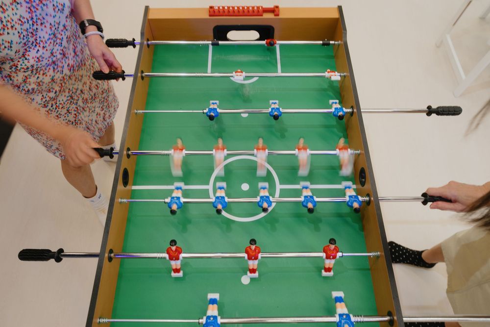 A sequence of close-up shots showing a foosball table gameplay with red and blue players on green playing surface.