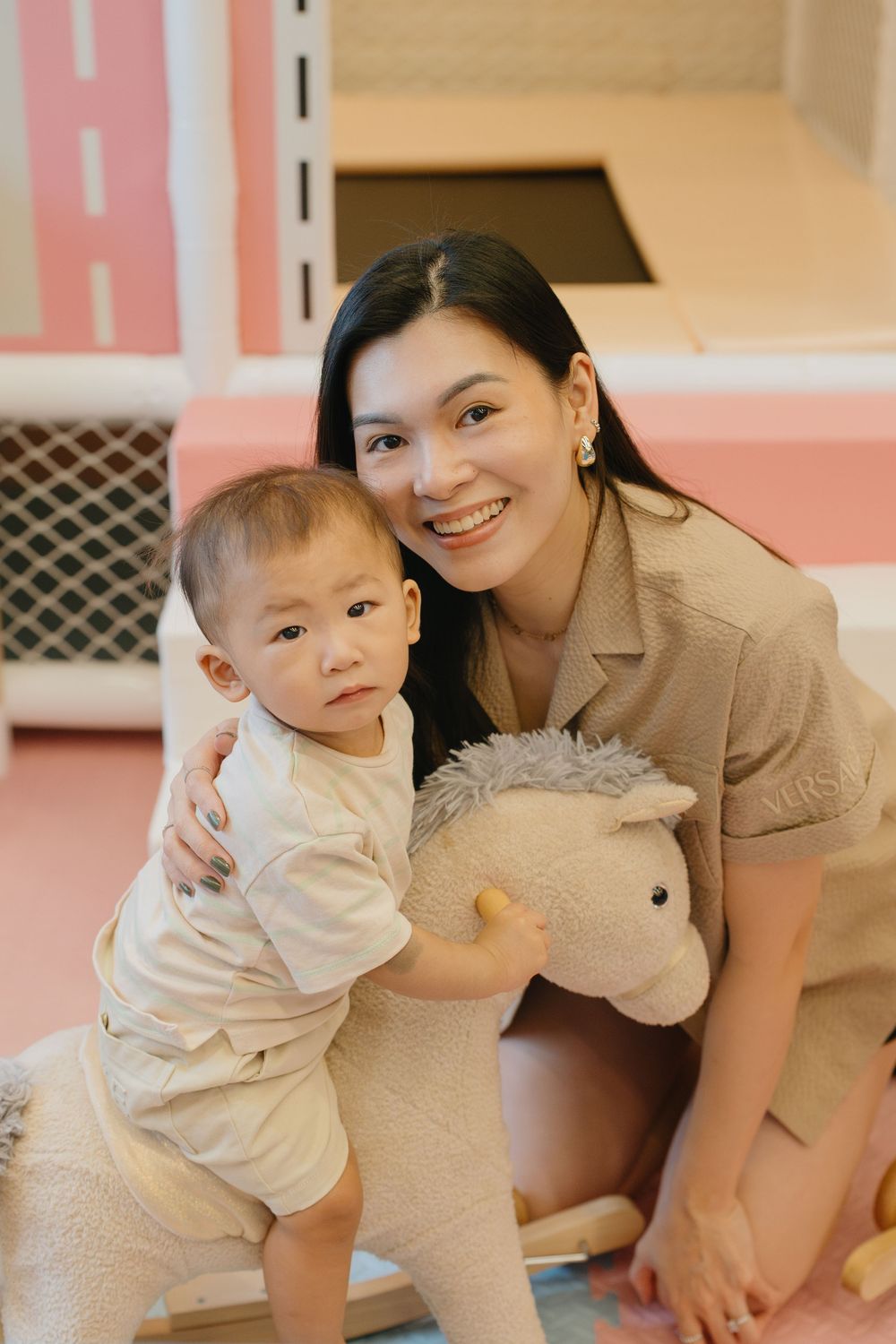 A toddler plays with a large plush elephant toy in a pink-walled room.