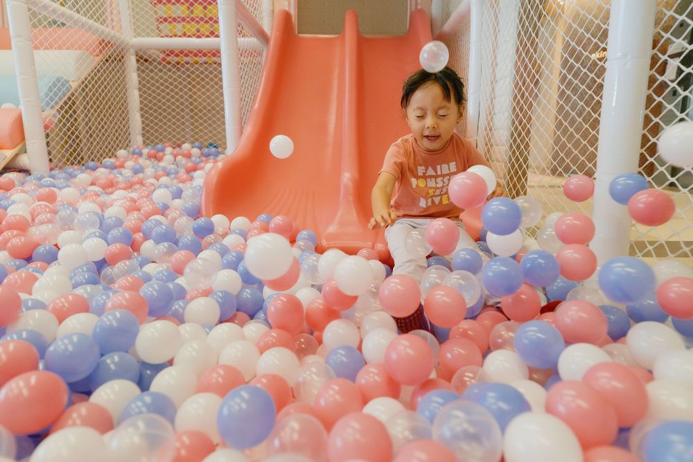 Pink and blue balloon pit filled with pastel colored balloons in an indoor play area with mesh barriers.