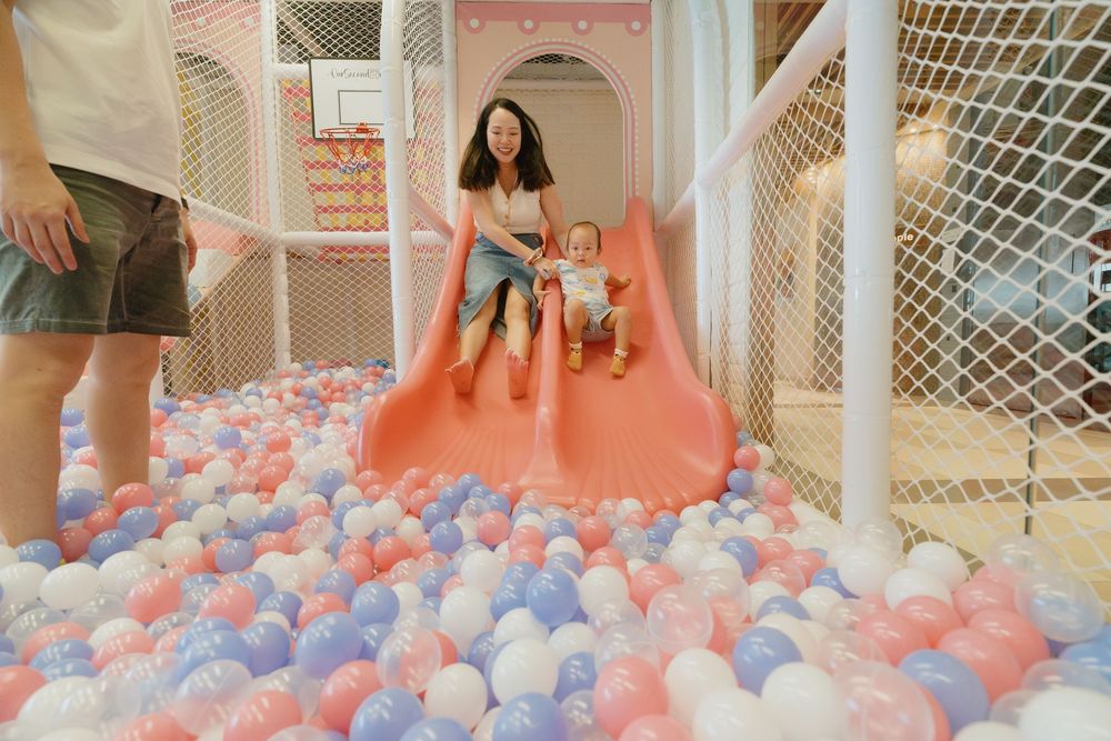 Children playing in a colorful ball pit filled with pink, blue and white balls at an indoor play area.