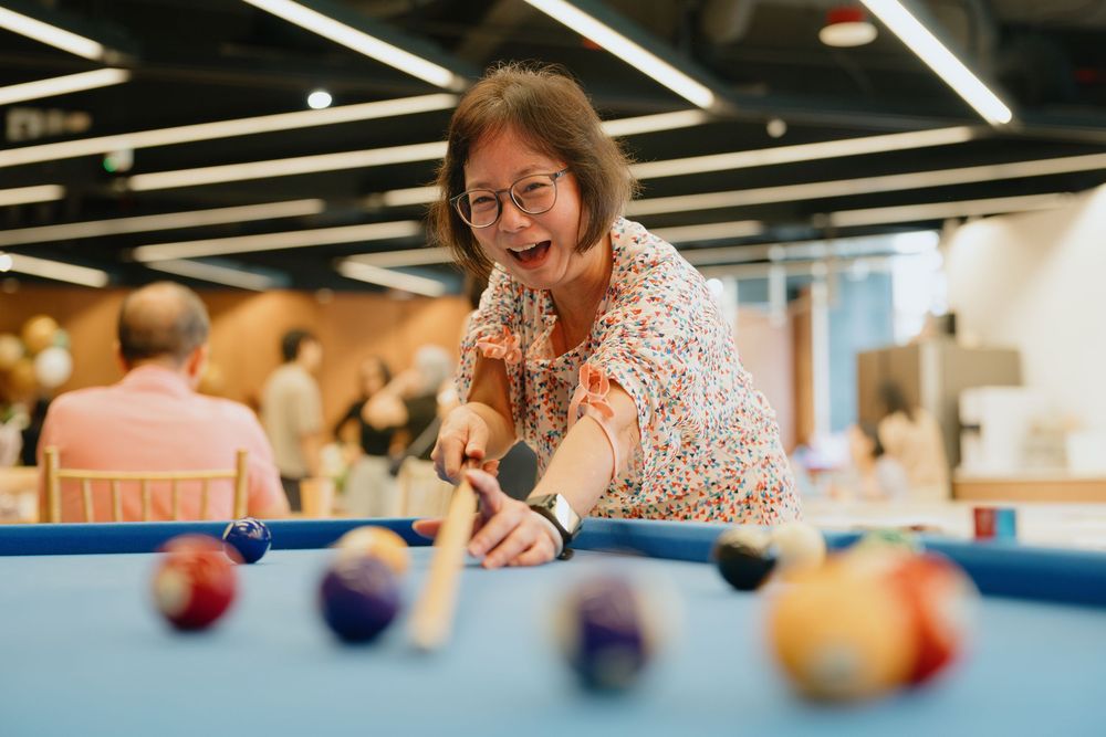 A person leans over a blue pool table, smiling while preparing to take a shot at colorful billiard balls.