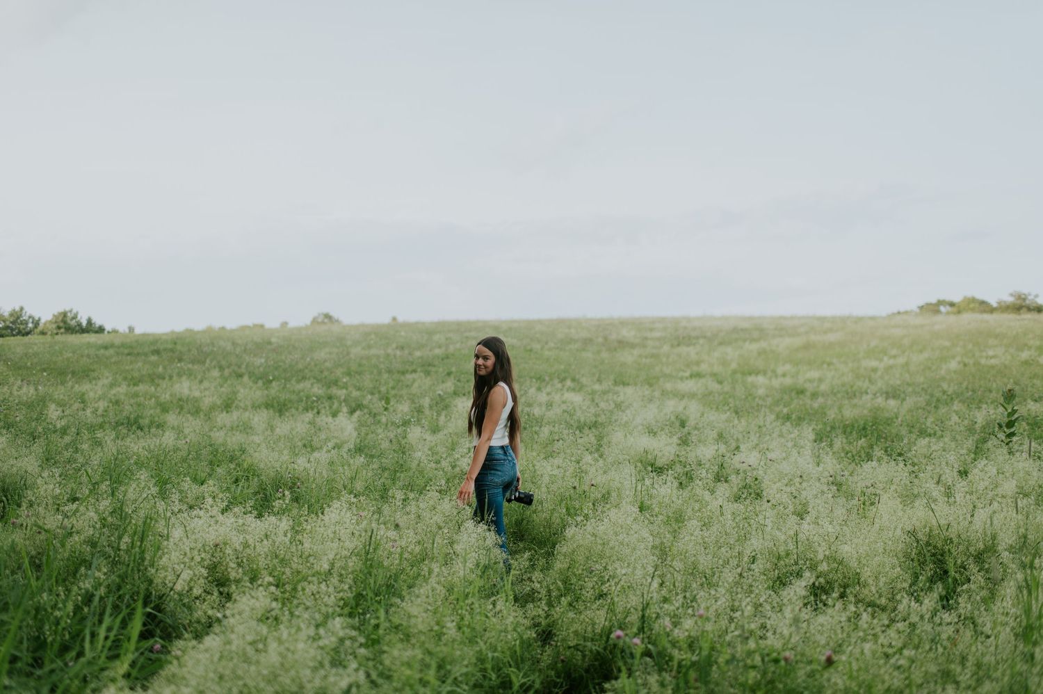 A person walks through a lush green meadow carrying a vintage suitcase on a sunny summer day.