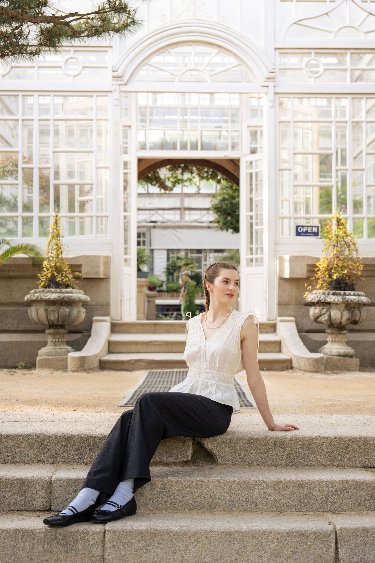 Elegant white conservatory entrance with decorative stone steps and ornate planters featuring golden holiday decorations.