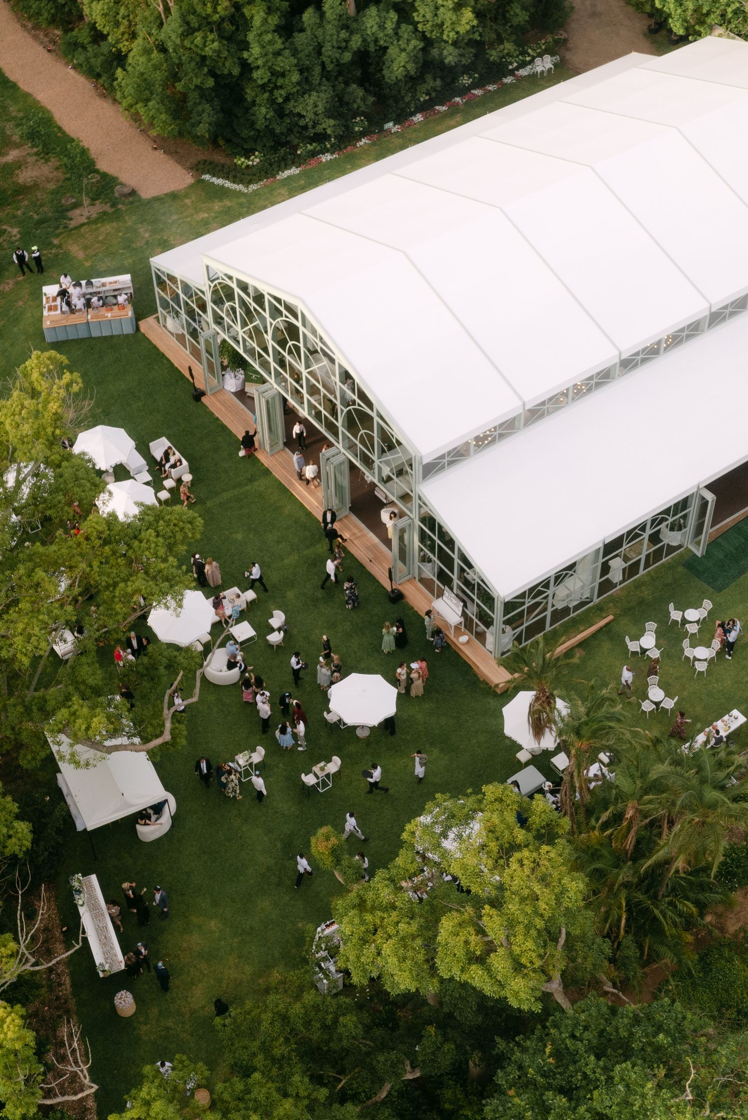 Aerial view of outdoor event tent and garden party setup with white canopies and green landscaping.