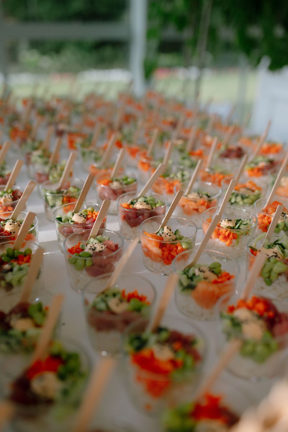 Rows of elegant appetizers in martini glasses arranged on a catering display with colorful garnishes and ingredients.