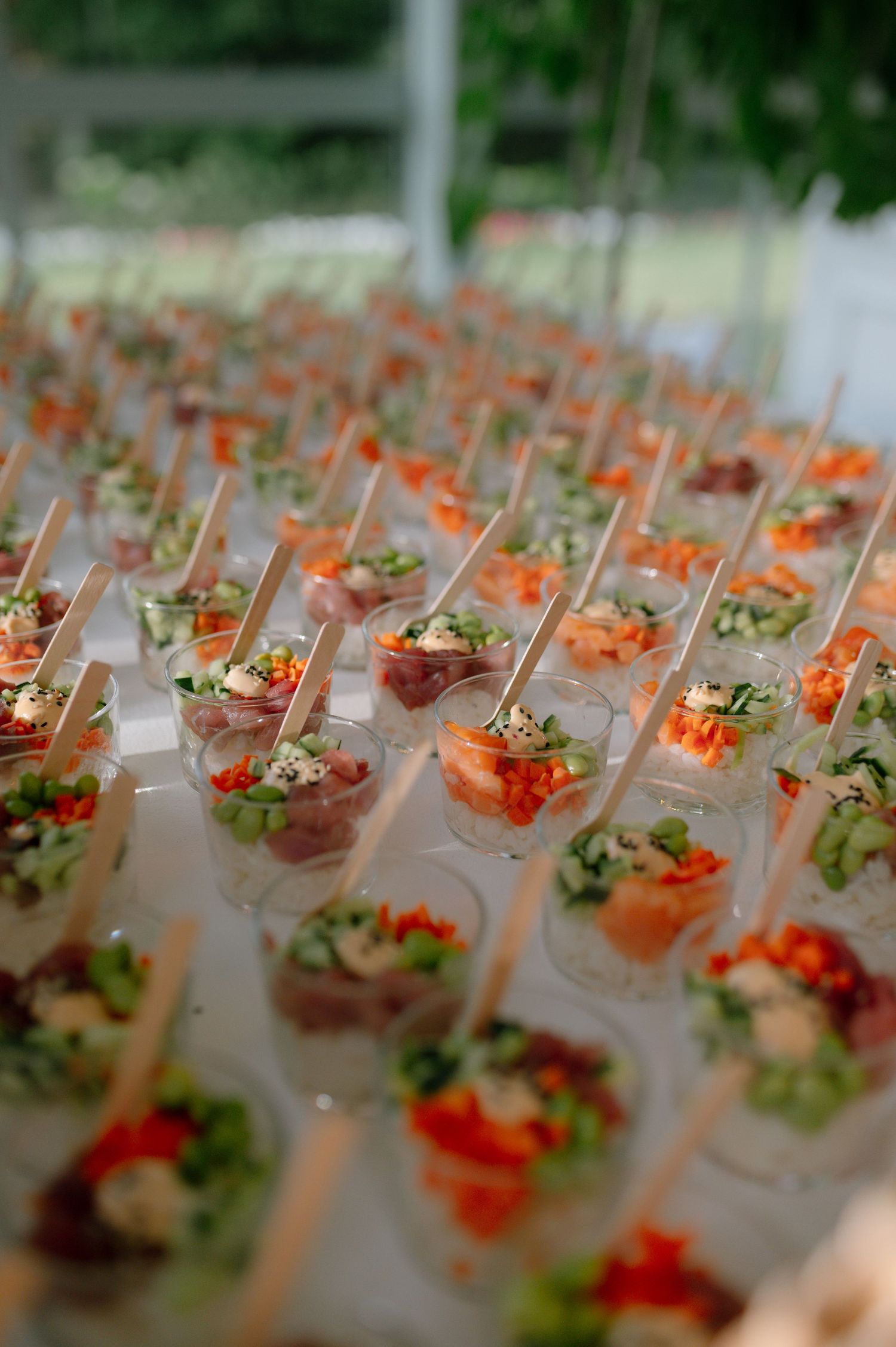 Rows of elegant appetizers in martini glasses arranged on a catering display with colorful garnishes and ingredients.
