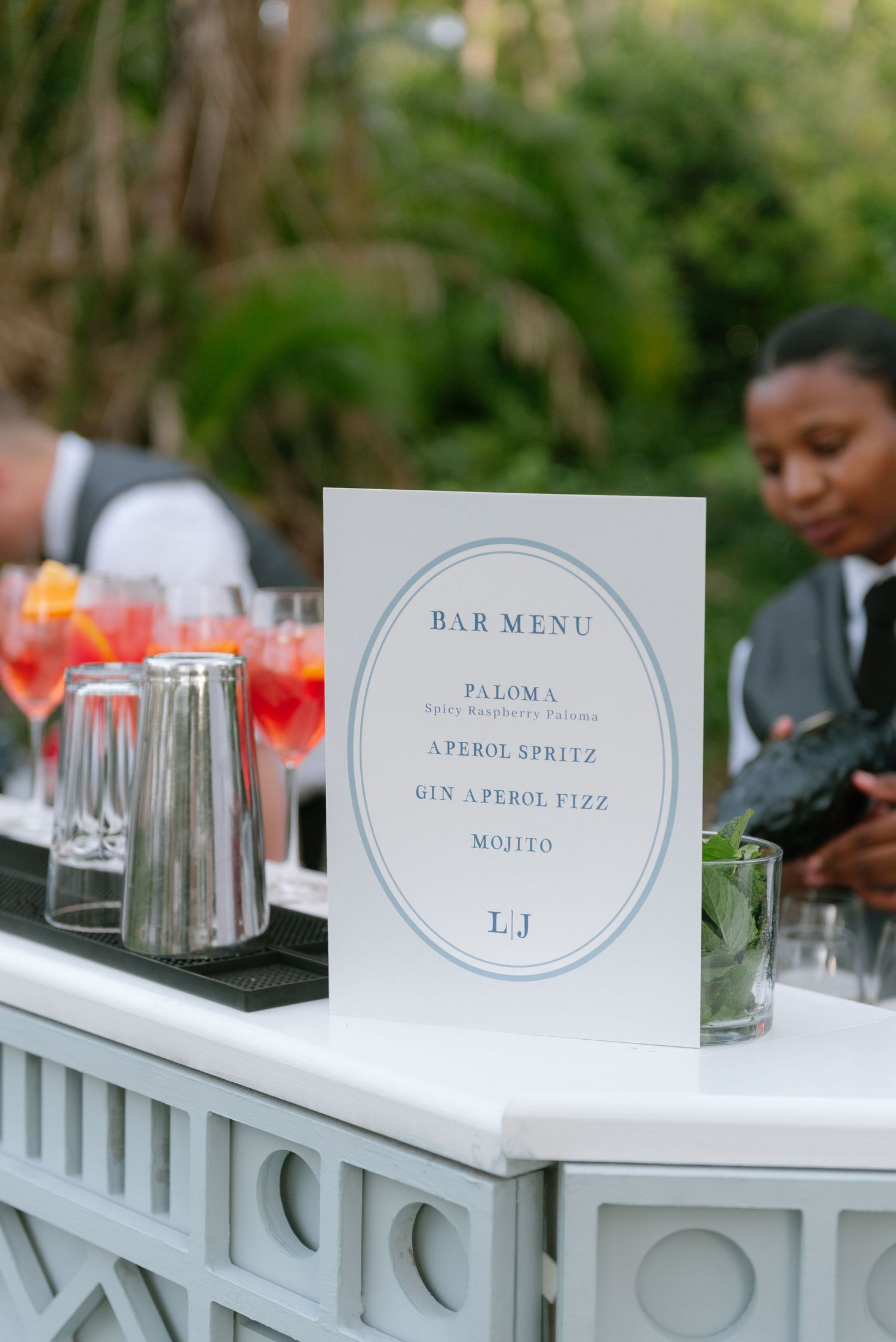 Bar menu cards and cocktail glasses line a white railing at an outdoor event setup.