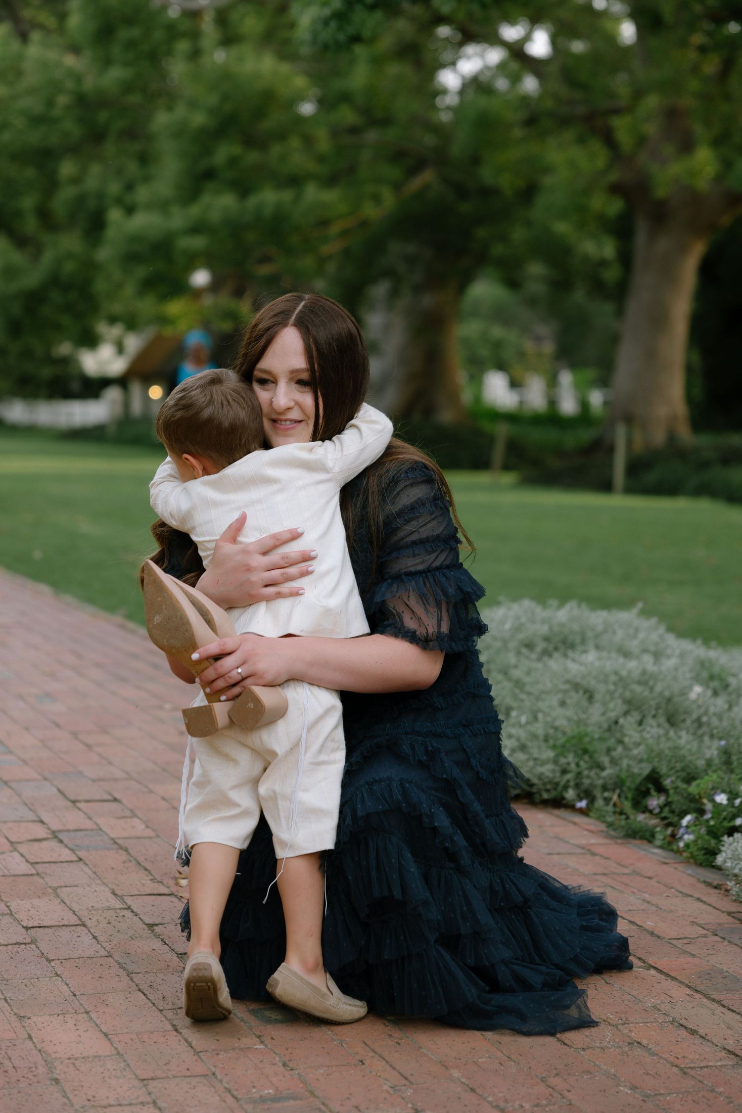 A tender moment captured in a garden setting as two people share an emotional embrace on a brick pathway.