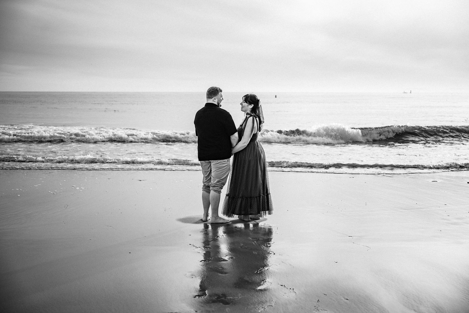 Couple standing with their backs to the camera looking at each other. the ocean behind them.