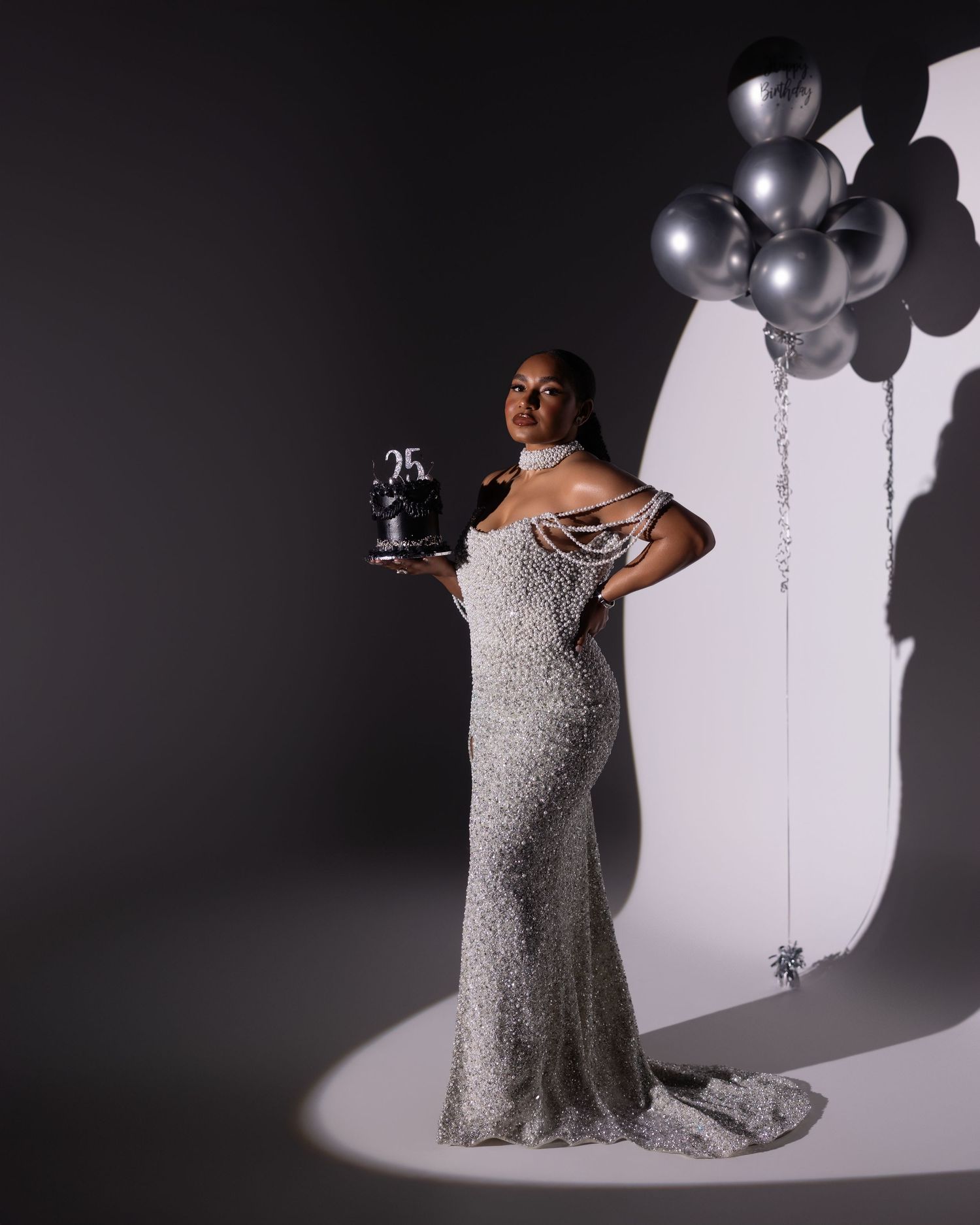 A figure in a sparkling silver gown poses elegantly with silver balloons against a dramatic monochrome backdrop.