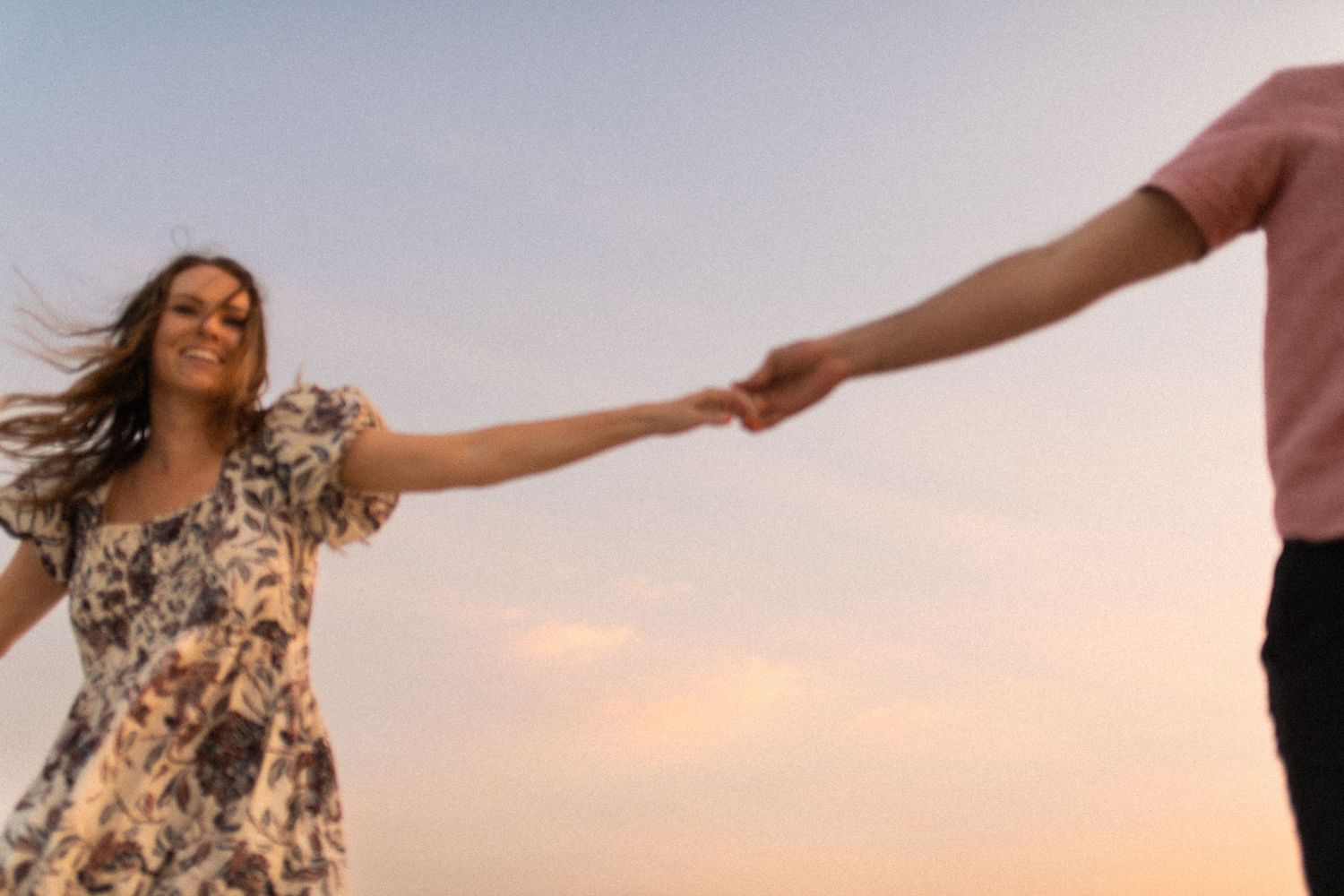 People dancing and twirling in floral dresses against a sunset sky.