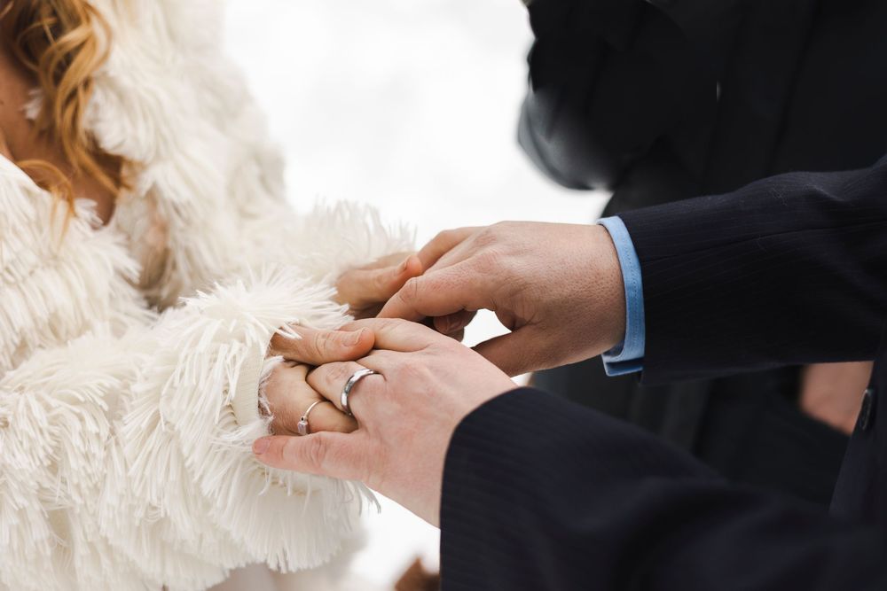 Close-up of groom placing wedding ring on bride's finger during winter ceremony, bride wearing white fur wrap.