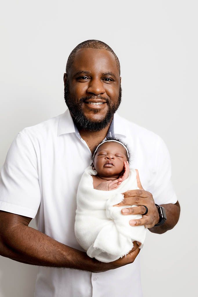 Smiling dad holding his swaddled newborn baby girl.