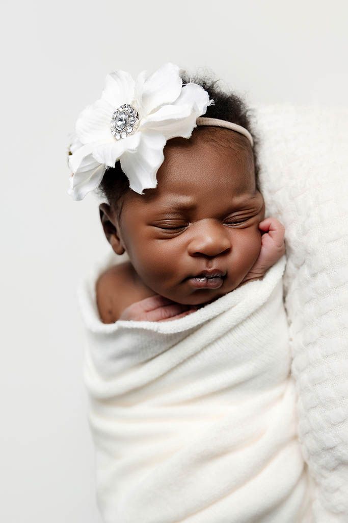 Hemet newborn photography of sleeping newborn baby girl swaddled in white wrap wearing a white flower headband.