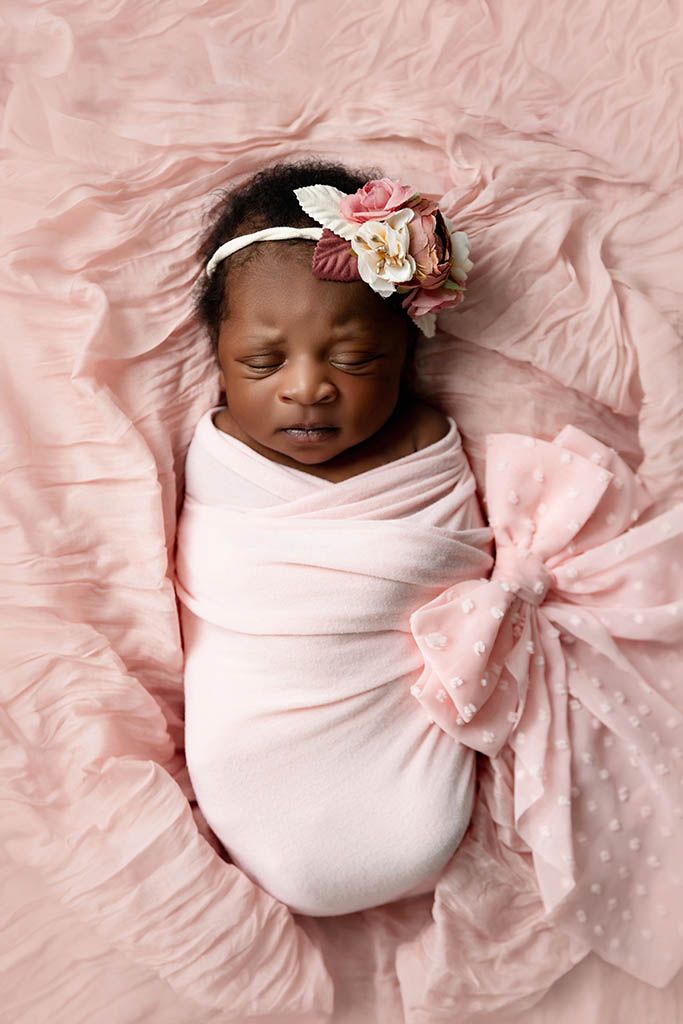 Newborn baby girl swaddled in pink wrap with a pink coquette bow.
