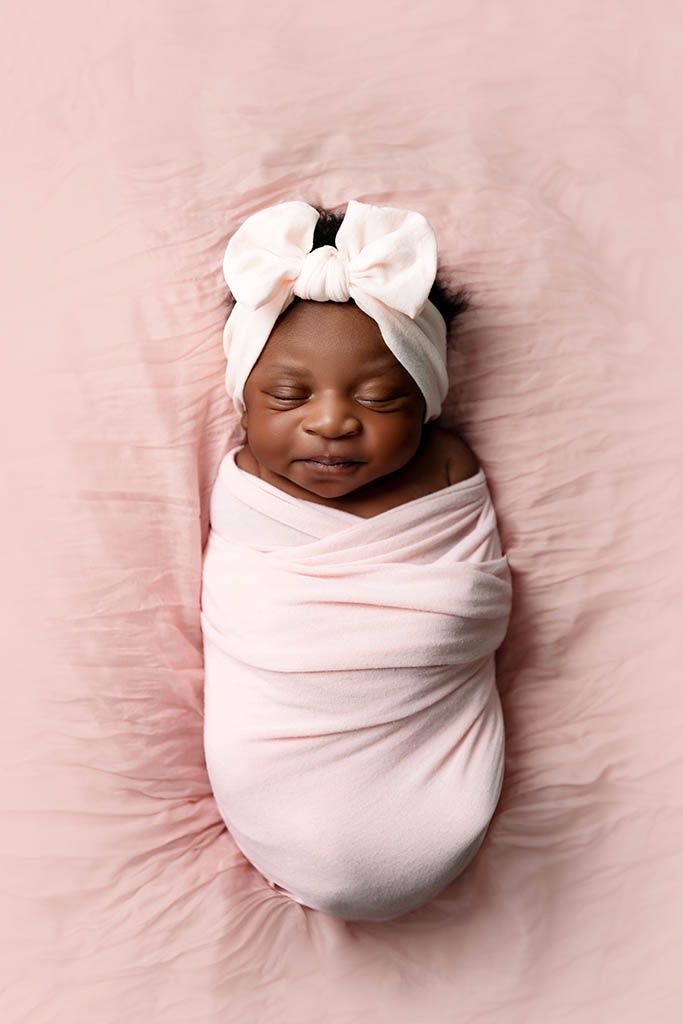 Newborn baby girl swaddled in pink wrap by Hemet newborn photographer.