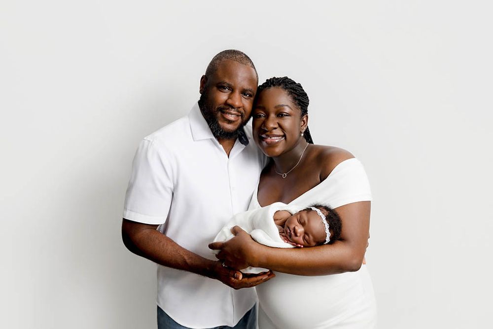 Smiling couple proudly holding their newborn baby against a white studio background.