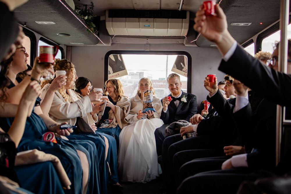 Wedding party celebrating on a party bus, bridesmaids in blue dresses toasting with red cups alongside bride and groom.