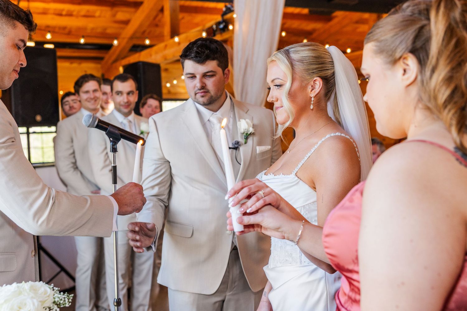 Bride and groom exchanging rings during indoor wedding ceremony with wedding party standing nearby.
