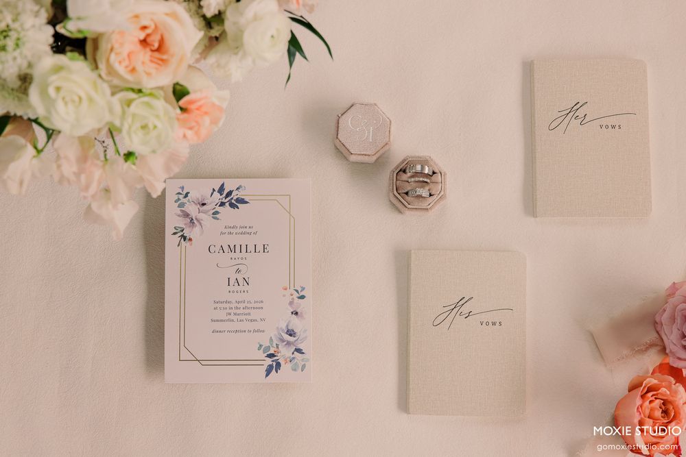 Elegant wedding stationery flat lay featuring floral invitations, ring box, and vow books on a soft blush background.
